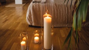 Une chambre à coucher avec un lit, une grande plante en pot et trois bougies allumées sur le plancher en bois.
