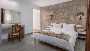 A modern hotel room with a large bed, a desk, and a chair. - Portiani Hotel (Milos)