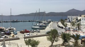 A marina with boats docked, a road leading to buildings, and a mountain in the background. - Portiani Hotel (Milos)