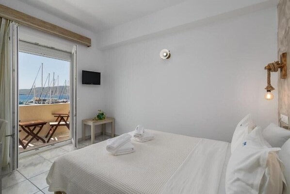 Habitación de hotel con cama, televisión, una mesita y vistas a barcos a través de una puerta corrediza.