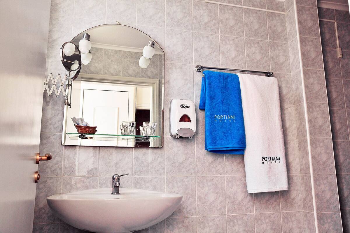 Une salle de bain avec un lavabo blanc, un miroir avec éclairage intégré, un porte-serviettes sur lequel est posée une serviette bleue, et un distributeur de savon Gojo.