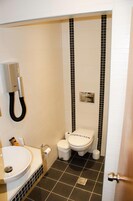 Un baño pequeño con un lavamanos blanco, un inodoro con etiqueta 'STERILIZED' y una zona de ducha con azulejos blancos y negros.