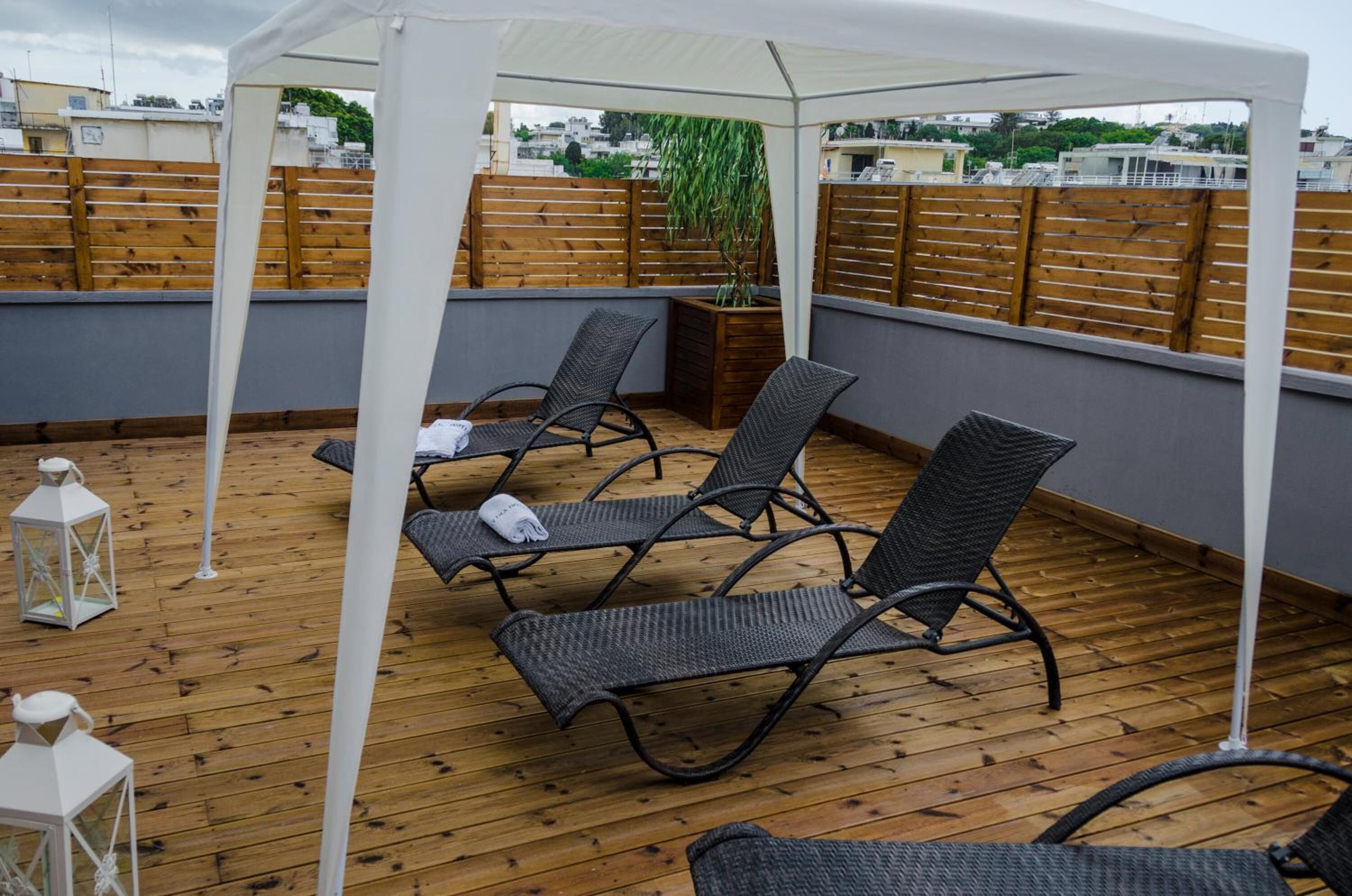 A rooftop terrace with wooden flooring, four wicker lounge chairs, a white canopy, and a wooden fence.