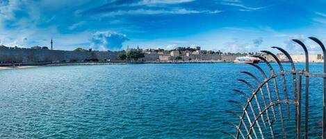 A coastal cityscape with a historic fortification, a clear blue sky, and a boat in the harbor.