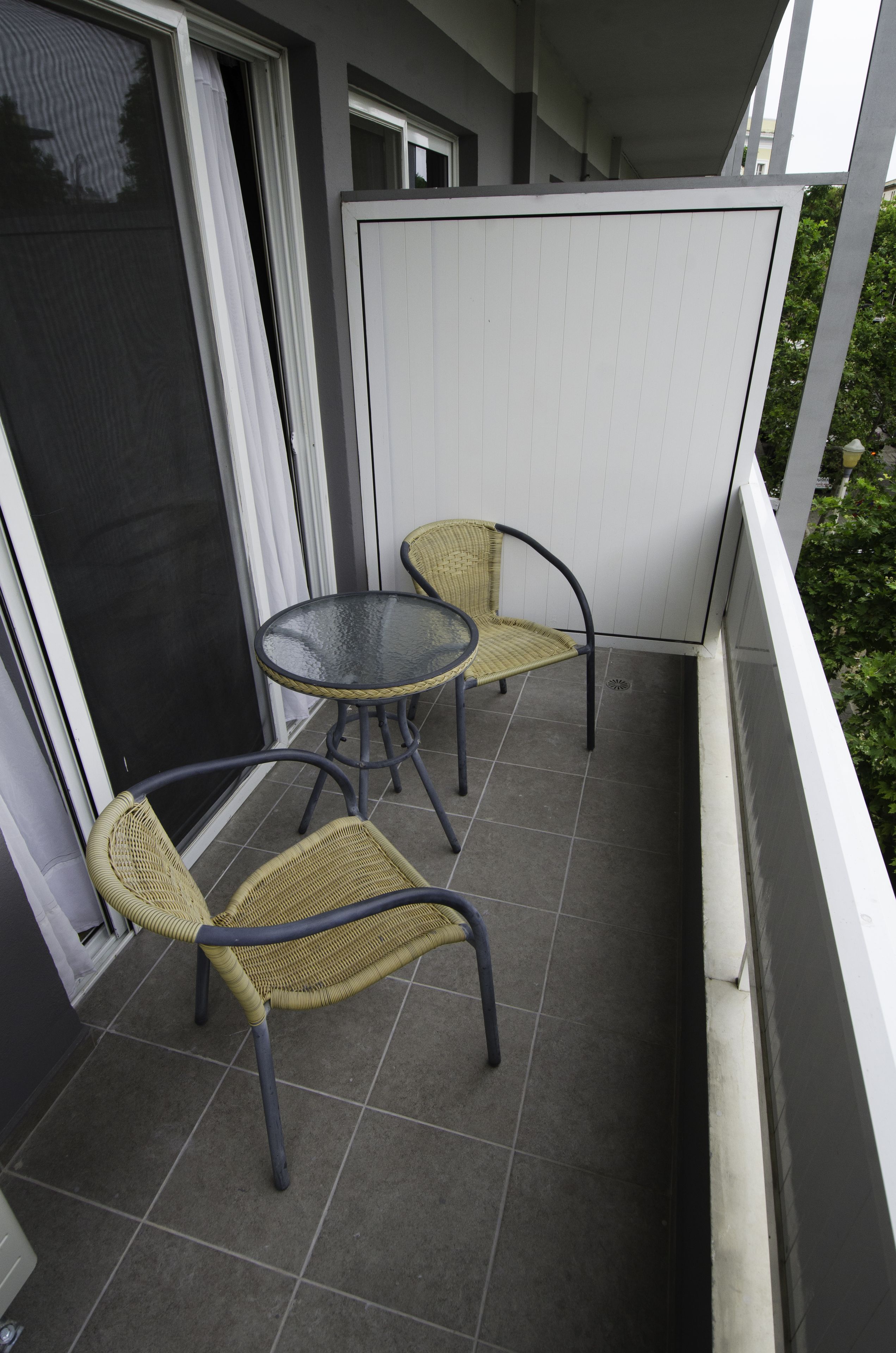 A balcony with two wicker chairs and a small round table.