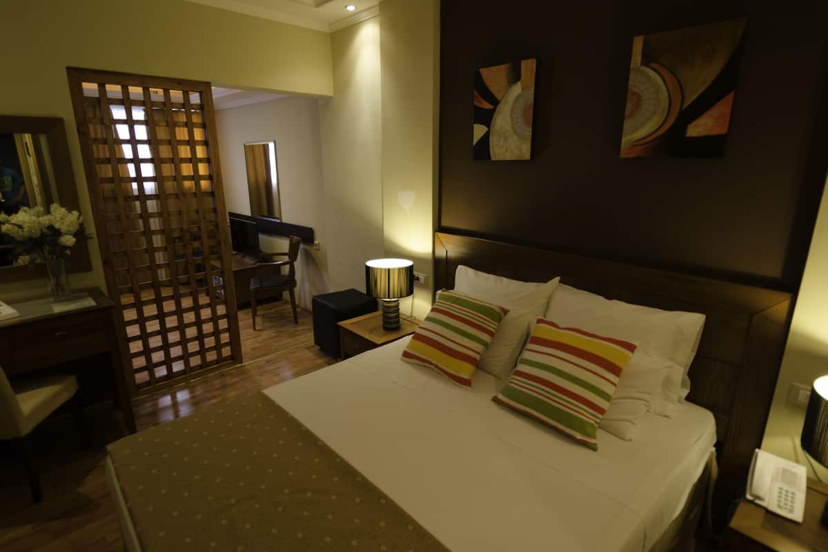 Una habitación de hotel con cama, mesita de noche, lámpara y un escritorio con silla.
