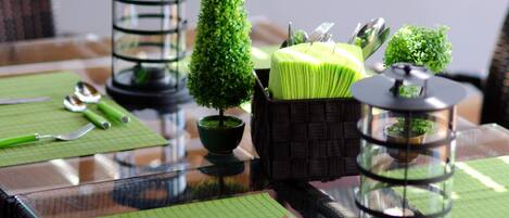 Une table à manger avec des sets de table verts, des couverts et des objets décoratifs, notamment de petites plantes en pot et une lanterne.