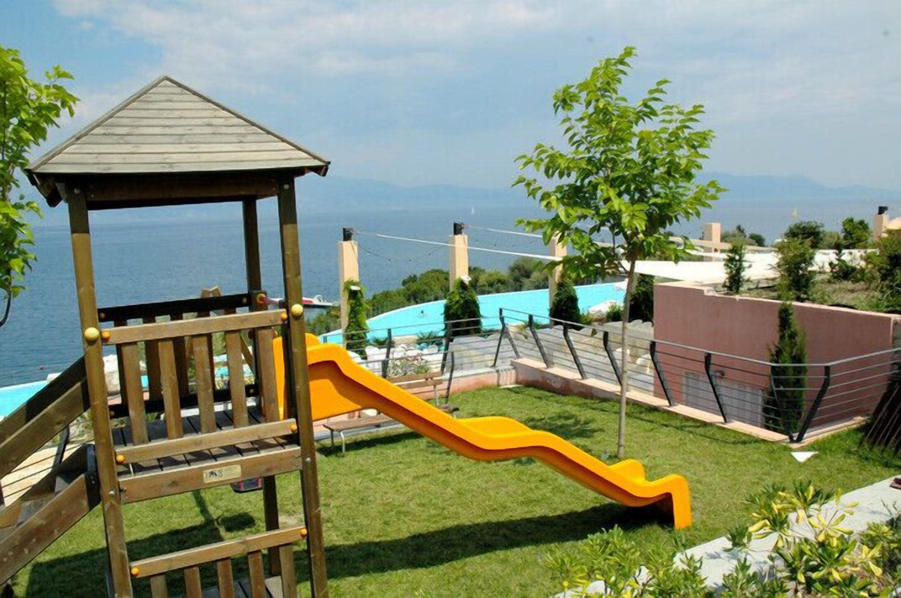 A wooden play structure with a slide, a small gazebo, and a pool in the background.