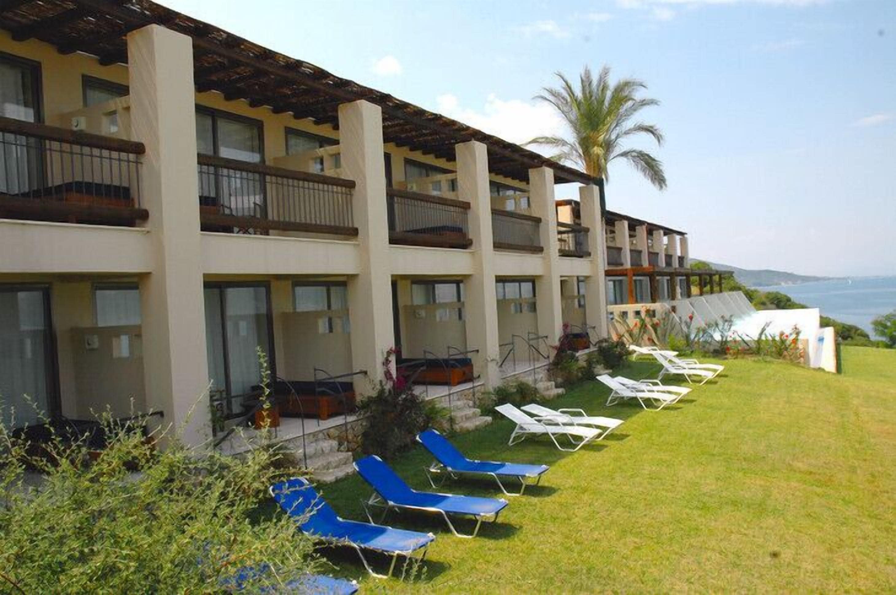 A hotel with multiple balconies, a pool area with sun loungers, and a view of the sea.