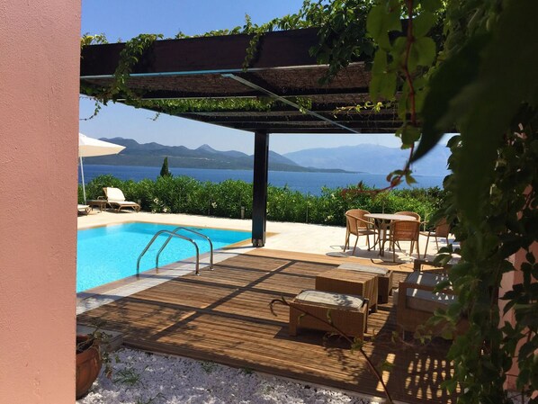 A poolside area with a wooden deck, lounge chairs, and a pergola with climbing plants. - Ionian Blue Bungalows And Spa Resort (Lefkada)