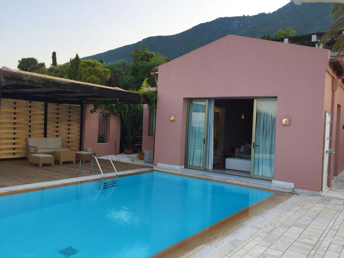 A swimming pool with a wooden deck and a pink building with a sliding glass door.