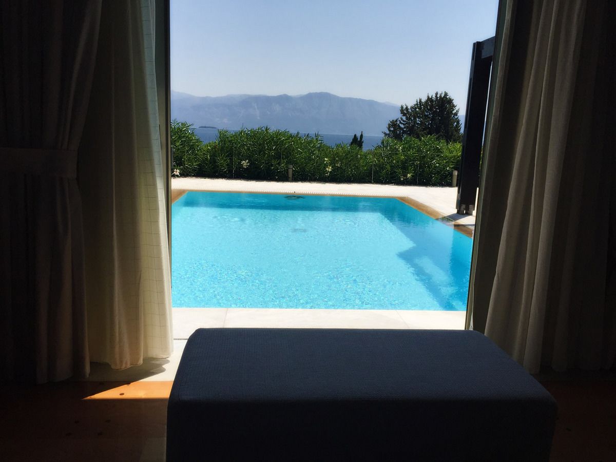 A view of a swimming pool with a mountain backdrop, curtains on either side, and a bench in the foreground.
