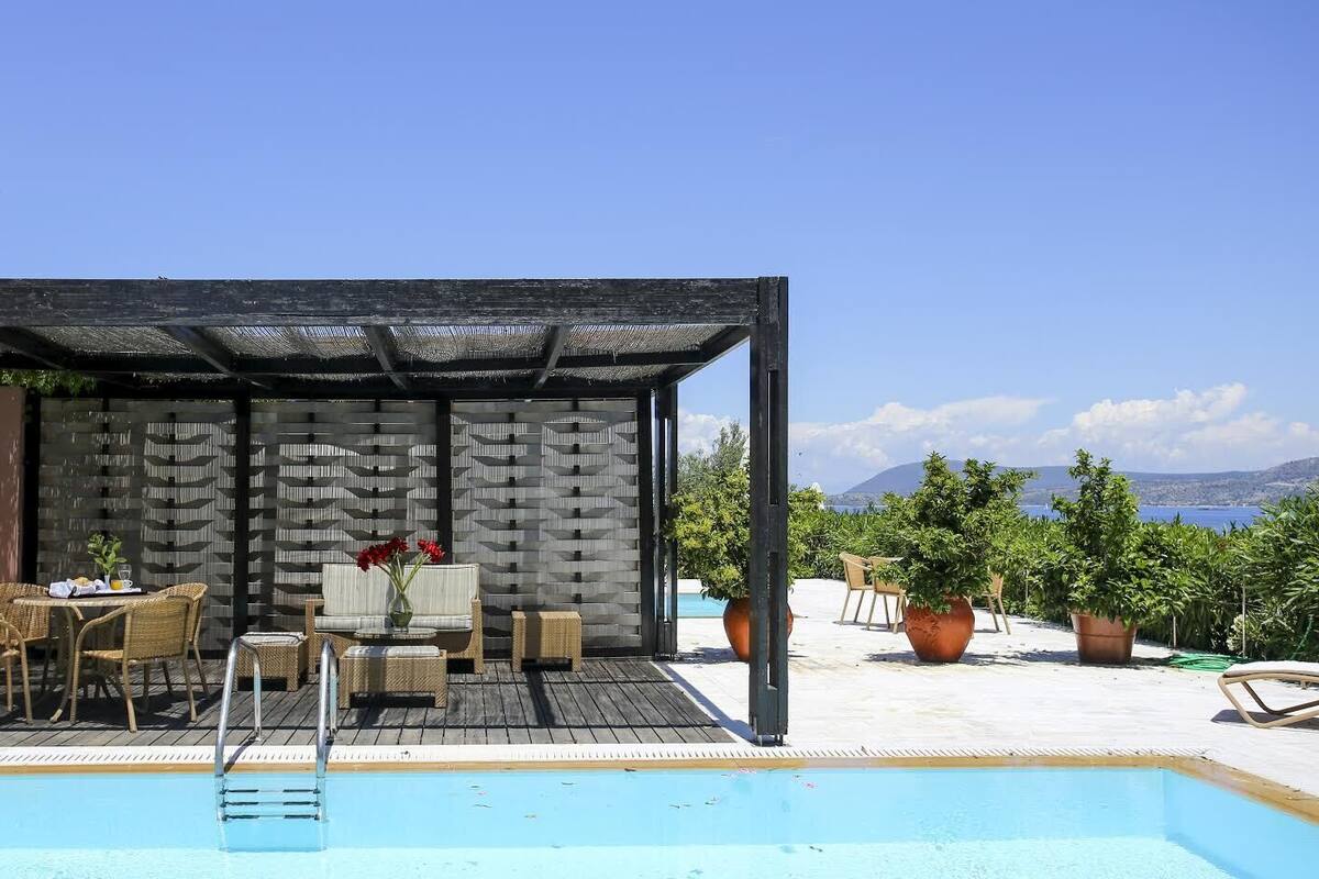 A poolside area with a covered seating area, a table with chairs, and potted plants.