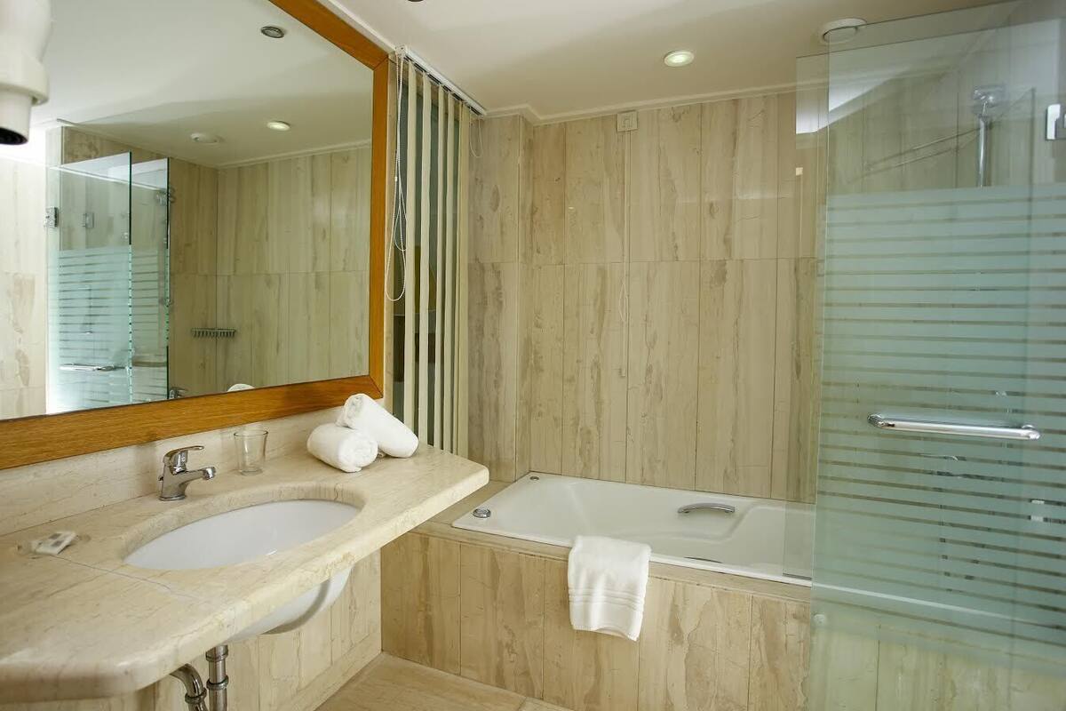 A modern bathroom with a large mirror, two sinks, a bathtub, and a glass shower enclosure.