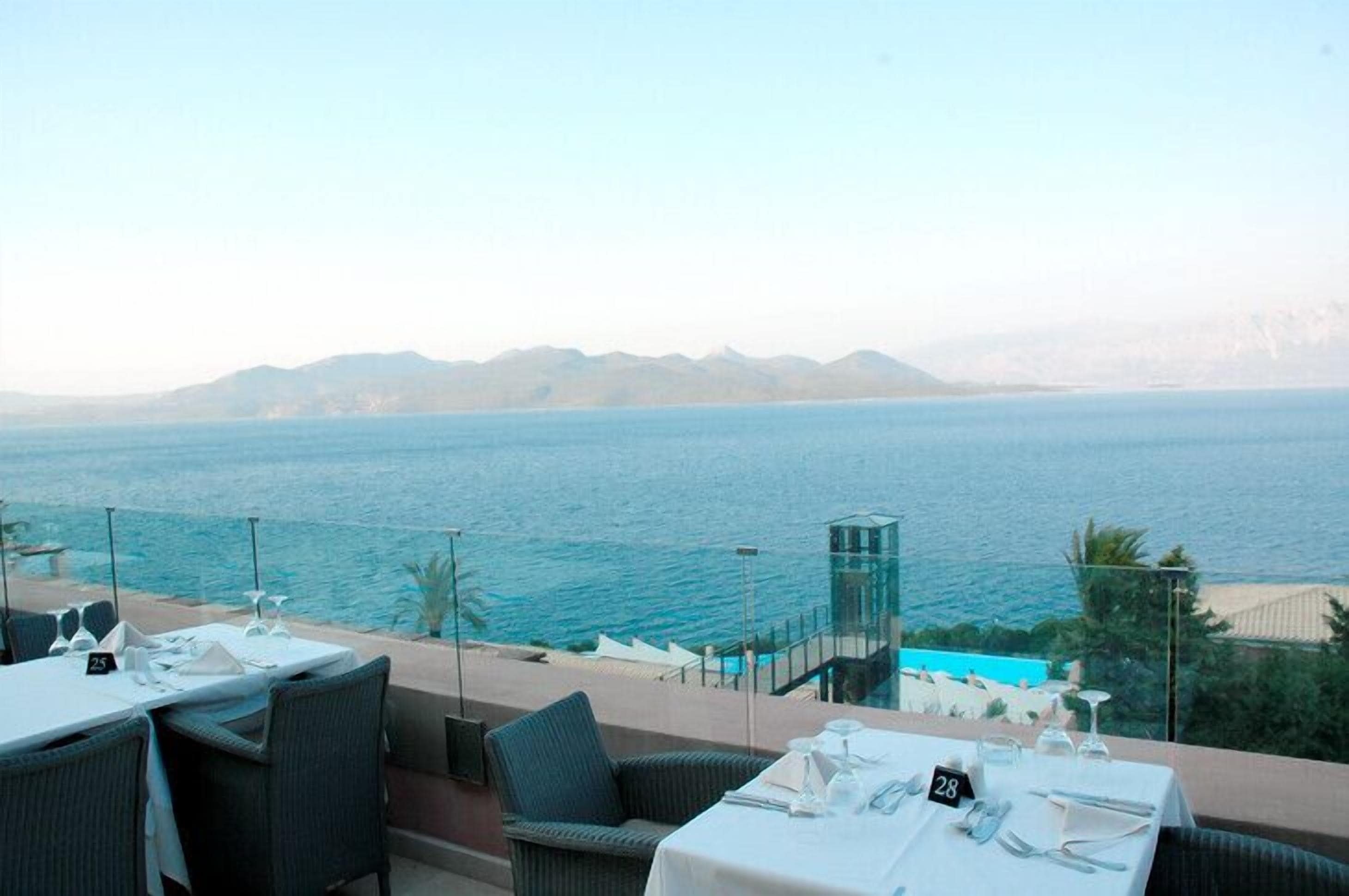 An outdoor dining area with tables set for two, overlooking a body of water and mountains.