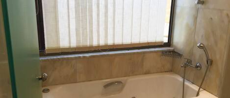 Un baño con bañera, ventana con persianas, ducha y retrete.