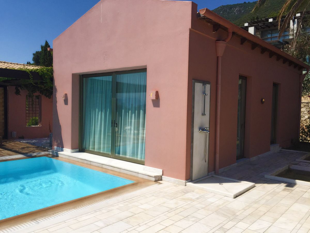 A modern building with a swimming pool, large sliding glass doors, and a stone pathway leading to a door.