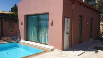 A modern building with a swimming pool, large sliding glass doors, and a stone pathway leading to a door.
