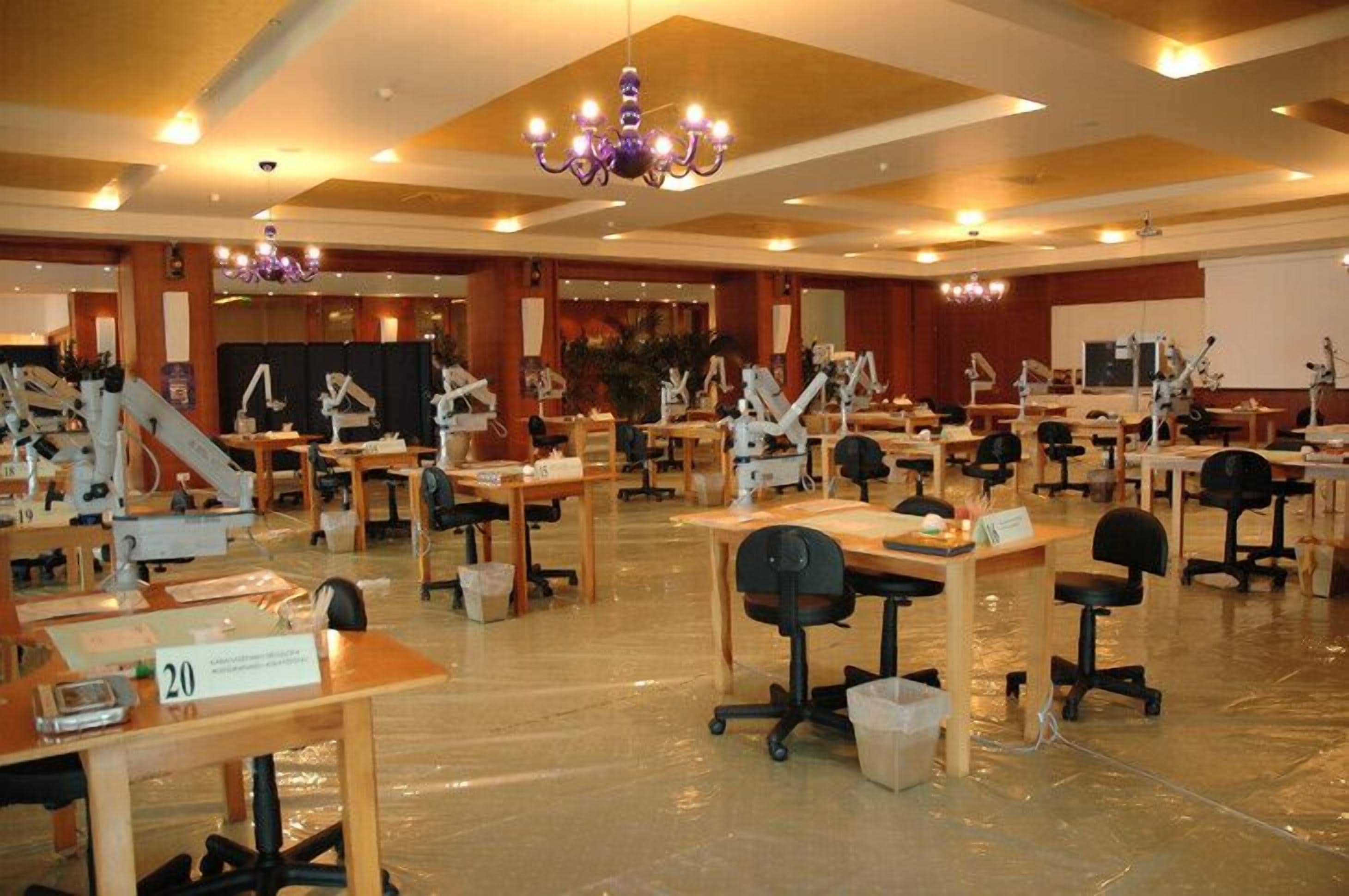 A large conference room with multiple tables and chairs, equipped with presentation screens and lighting.