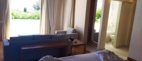 A hotel room with a bed, a sofa, a small table, and a view of the outdoors.