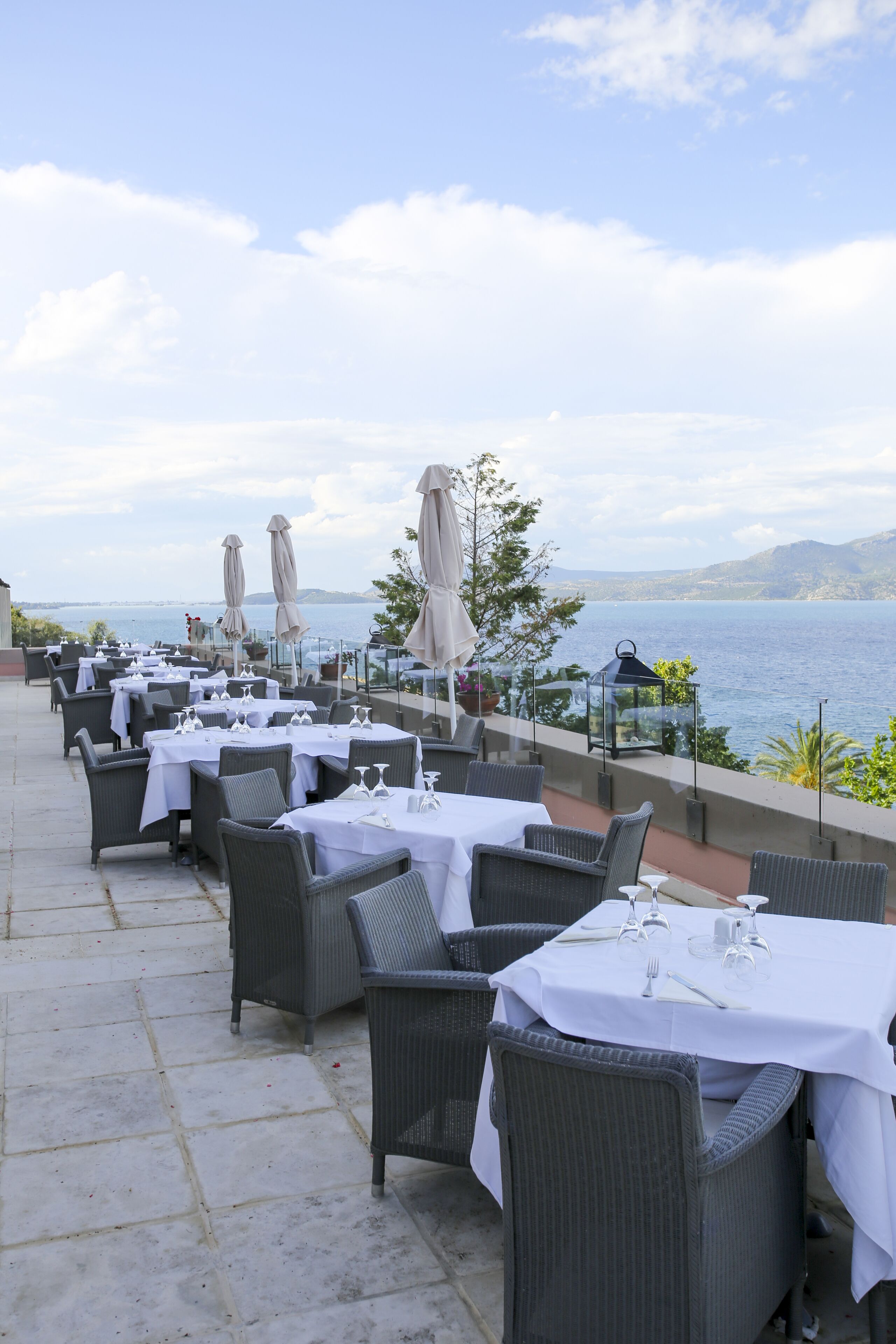 Un área de comedor al aire libre con mesas dispuestas para dos, con vista a un cuerpo de agua.