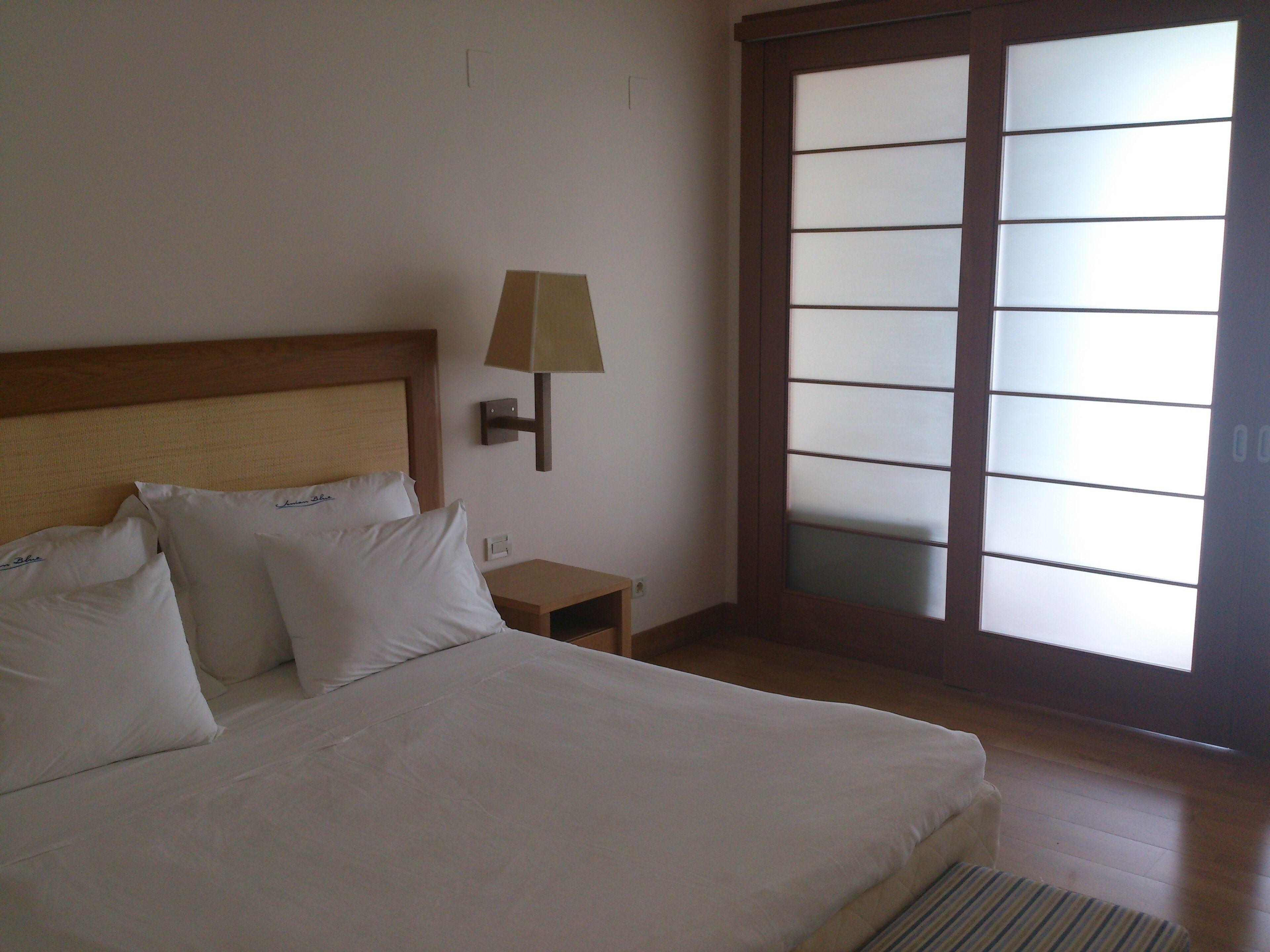 Una habitación de hotel con cama, mesita de noche, lámpara y puerta corrediza de cristal.