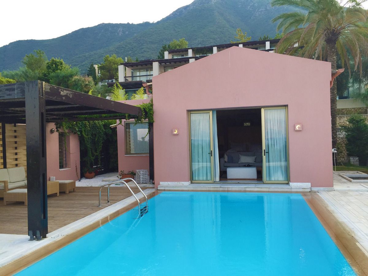 A swimming pool with a wooden deck, a pink building with a sliding glass door, and a mountain in the background.