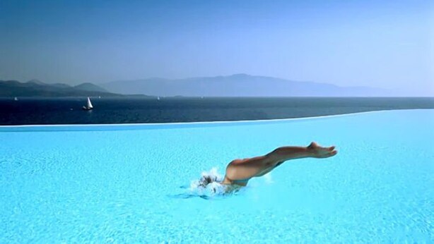 A person diving into a clear blue pool with a view of mountains in the background. - Ionian Blue Bungalows And Spa Resort (Lefkada)