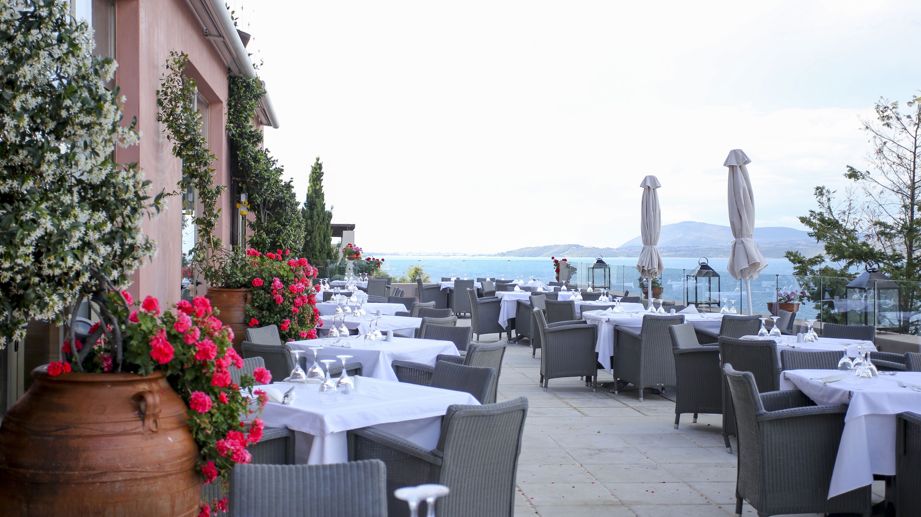 An outdoor dining area with tables set for guests, overlooking a body of water.