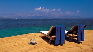 A wooden deck with two sun loungers and a table with a bottle and glass. - Ionian Blue Bungalows And Spa Resort (Lefkada)