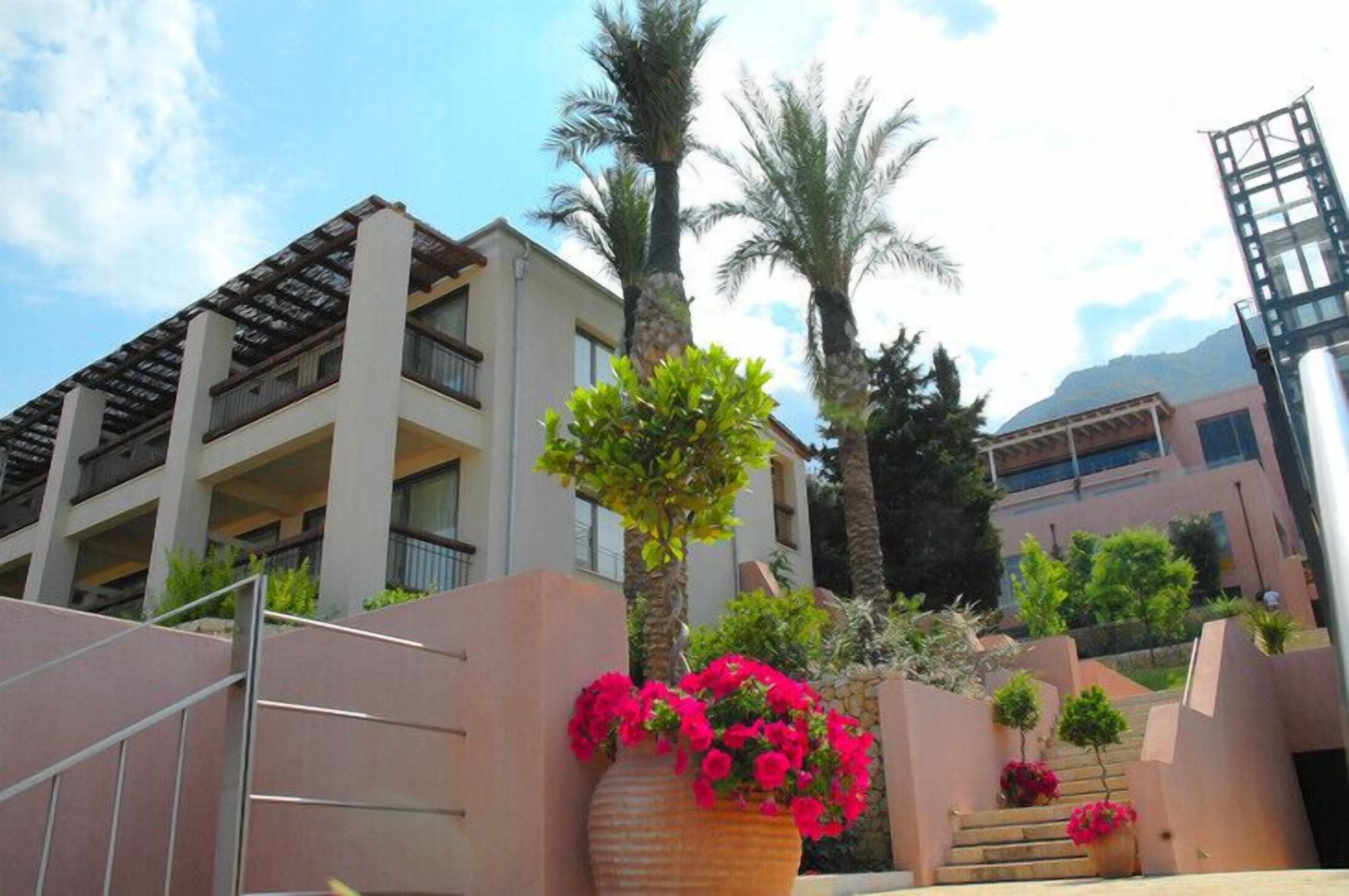 A multi-story hotel with balconies, palm trees, and a staircase leading to the entrance.