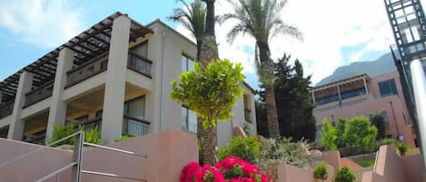 A multi-story hotel with balconies, palm trees, and a staircase leading to the entrance.