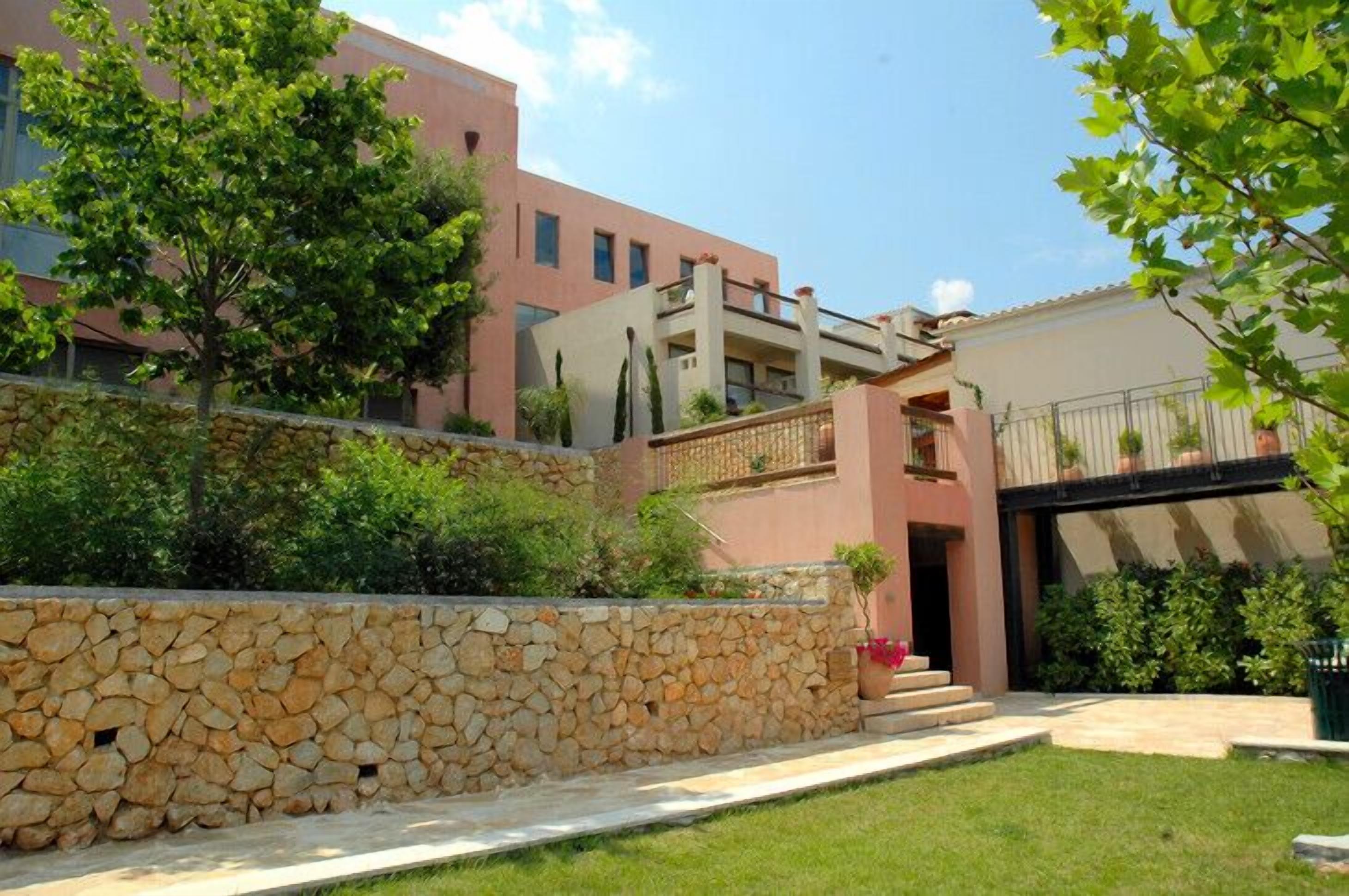 Un edificio moderno con pared de piedra, balcón y jardín bien cuidado.