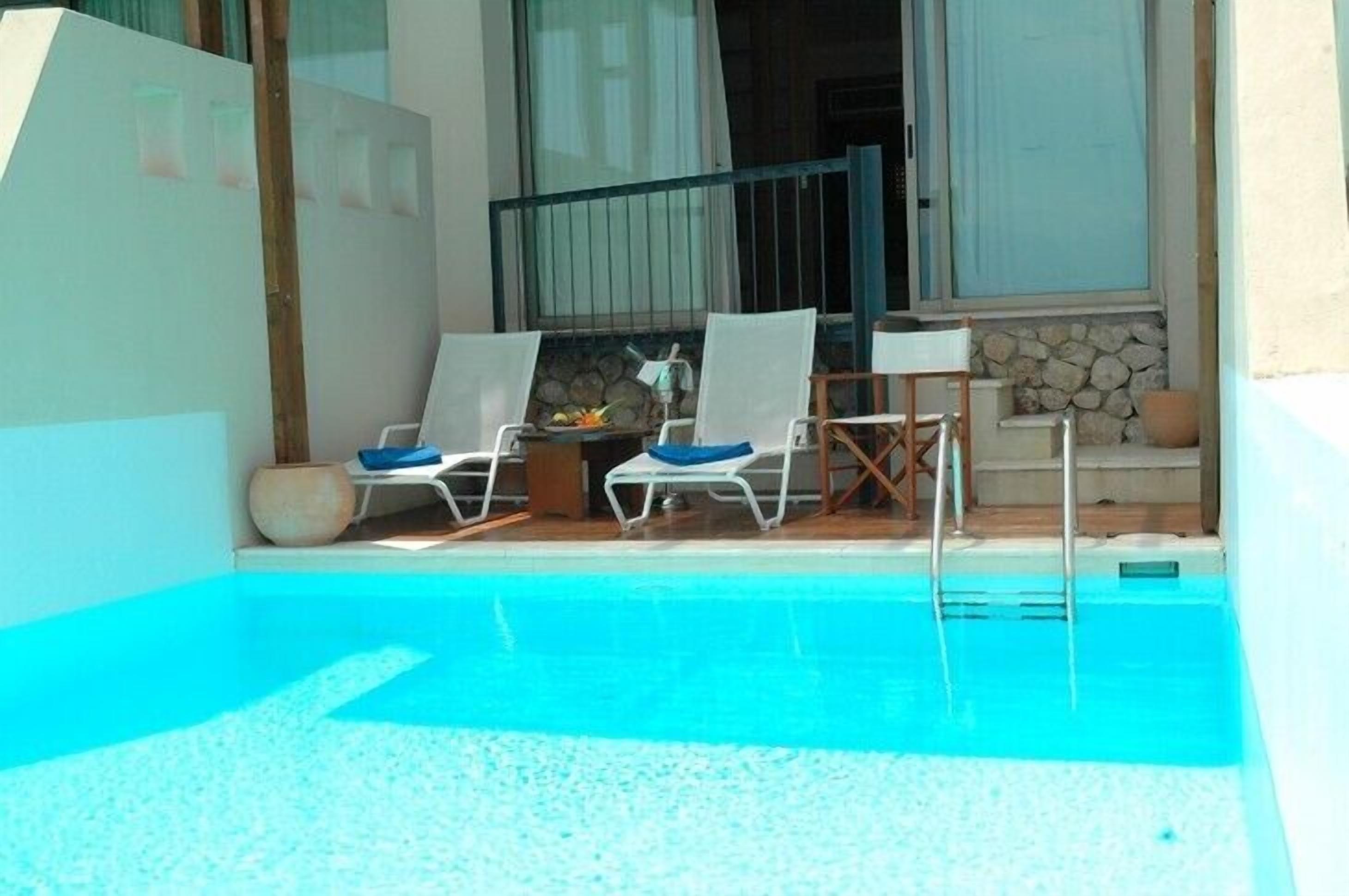 Area piscina con due lettini e un tavolo, un muro in pietra e una finestra con tende.