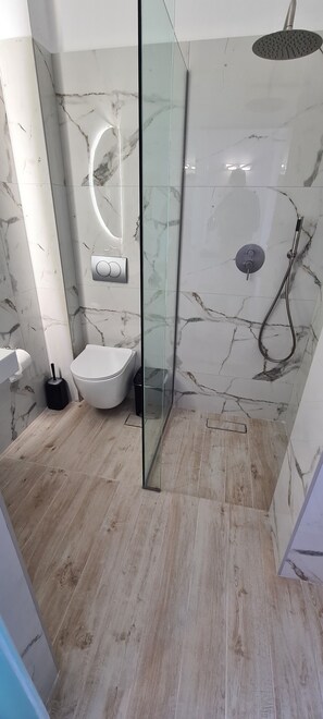 Une salle de bain moderne avec une douche à parois de verre, un mur recouvert de carreaux de marbre, des toilettes blanches et un plancher en bois.