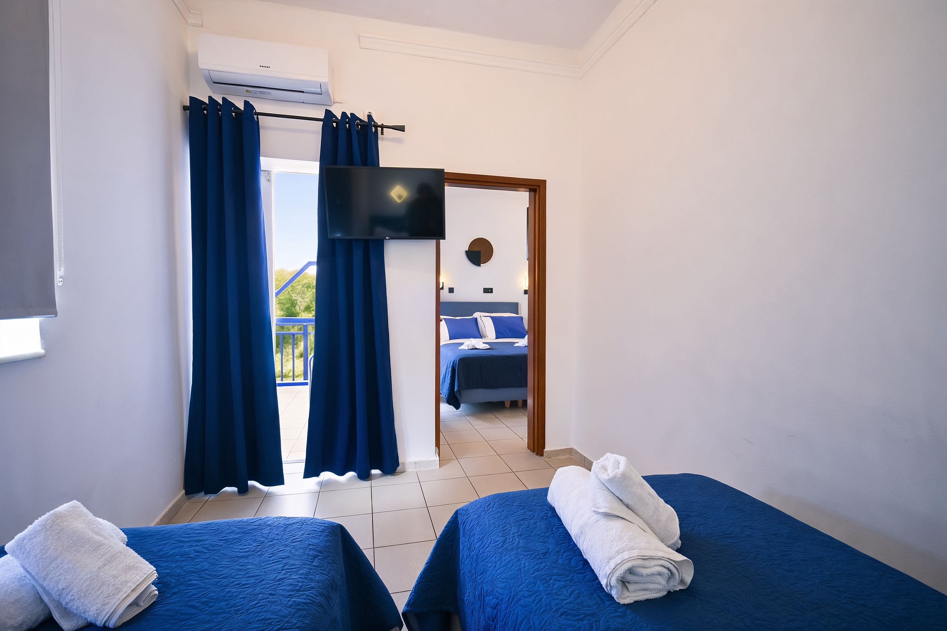 Hotellihuone, jossa on kaksi sänkyä, televisio ja parveke, jossa on verhot.
