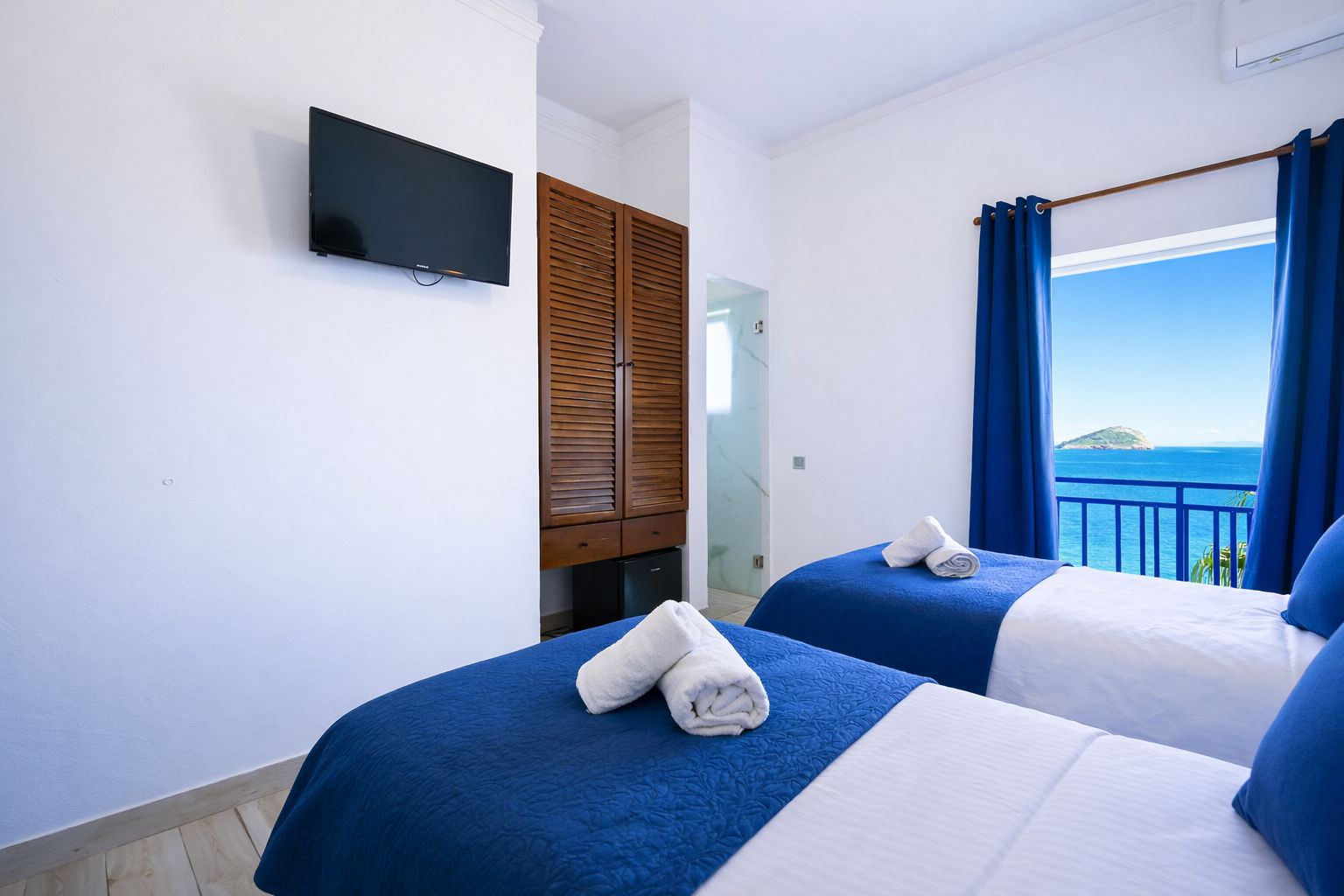 A hotel room with two beds, a TV, and a view of the sea.