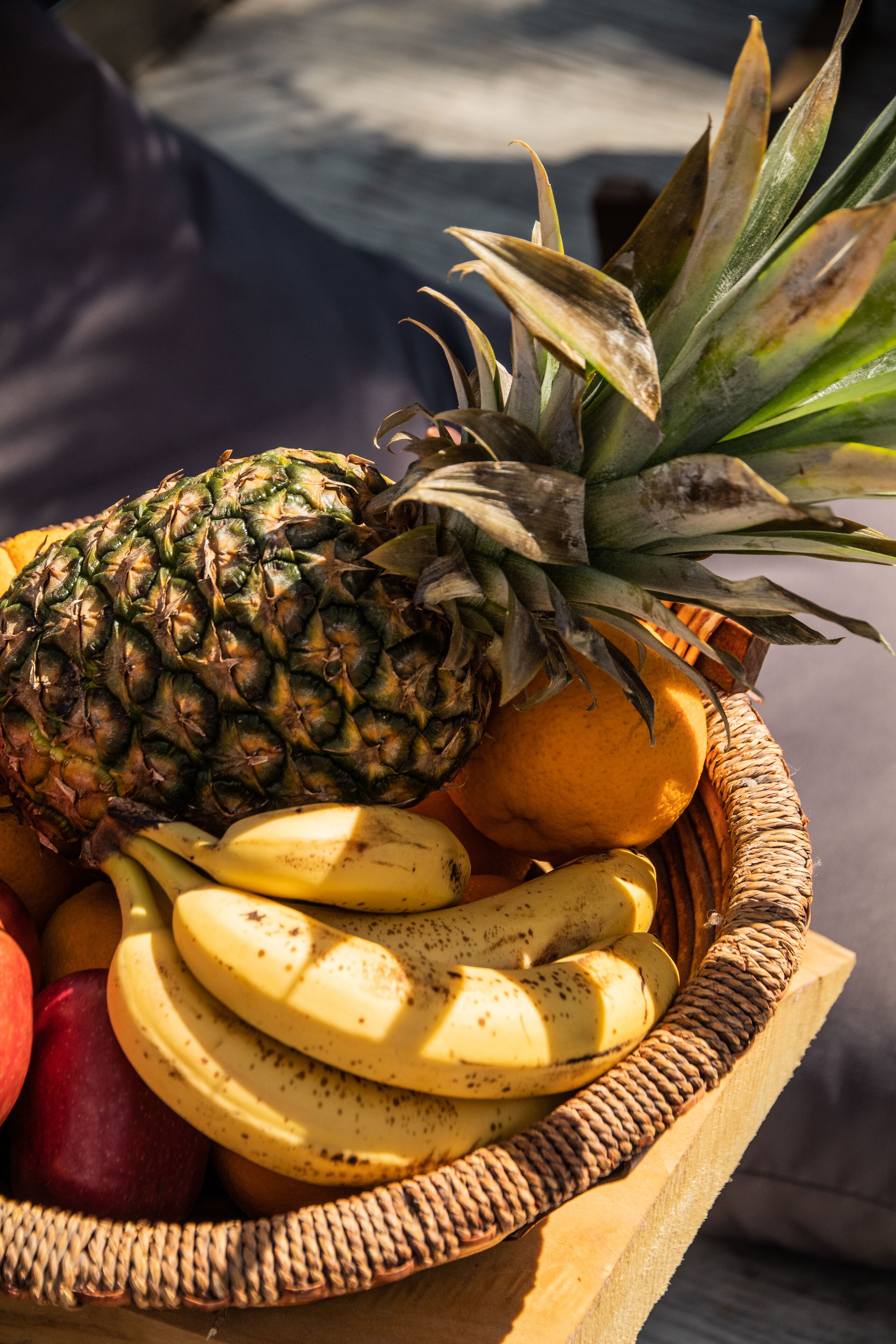 Una cesta de mimbre con una piña, plátanos, una naranja y manzanas.