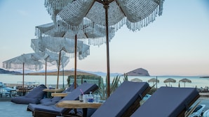 Ein Poolbereich mit Liegestühlen, Sonnenschirmen und Blick aufs Meer.