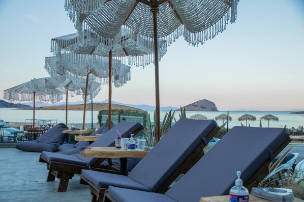 Un espace aménagé au bord de la piscine, avec des chaises longues, des parasols et une vue sur la mer.