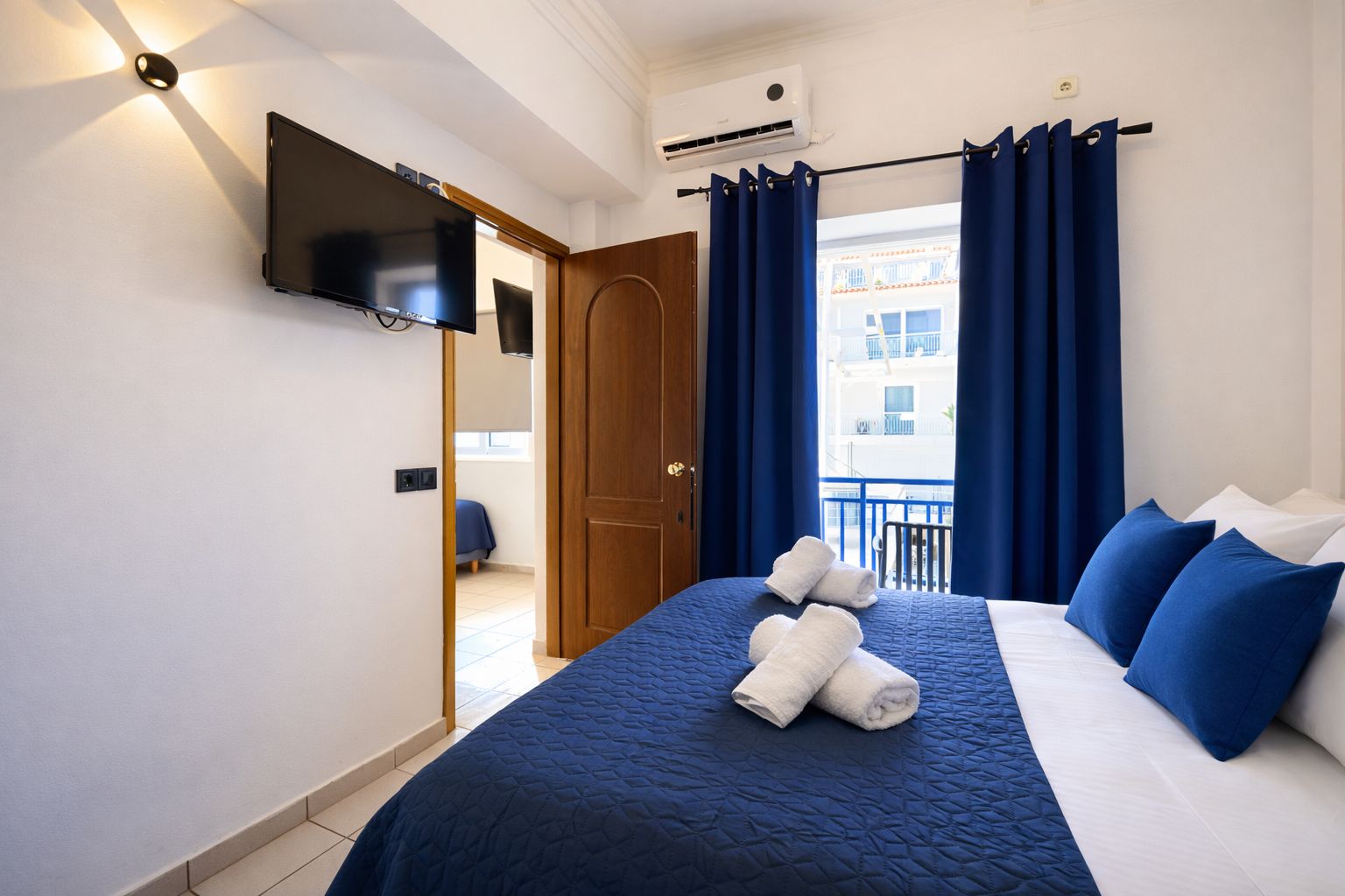 Une chambre d’hôtel équipée d’un lit, d’un téléviseur à écran plat, d’un balcon avec des rideaux et d’un système de climatisation.