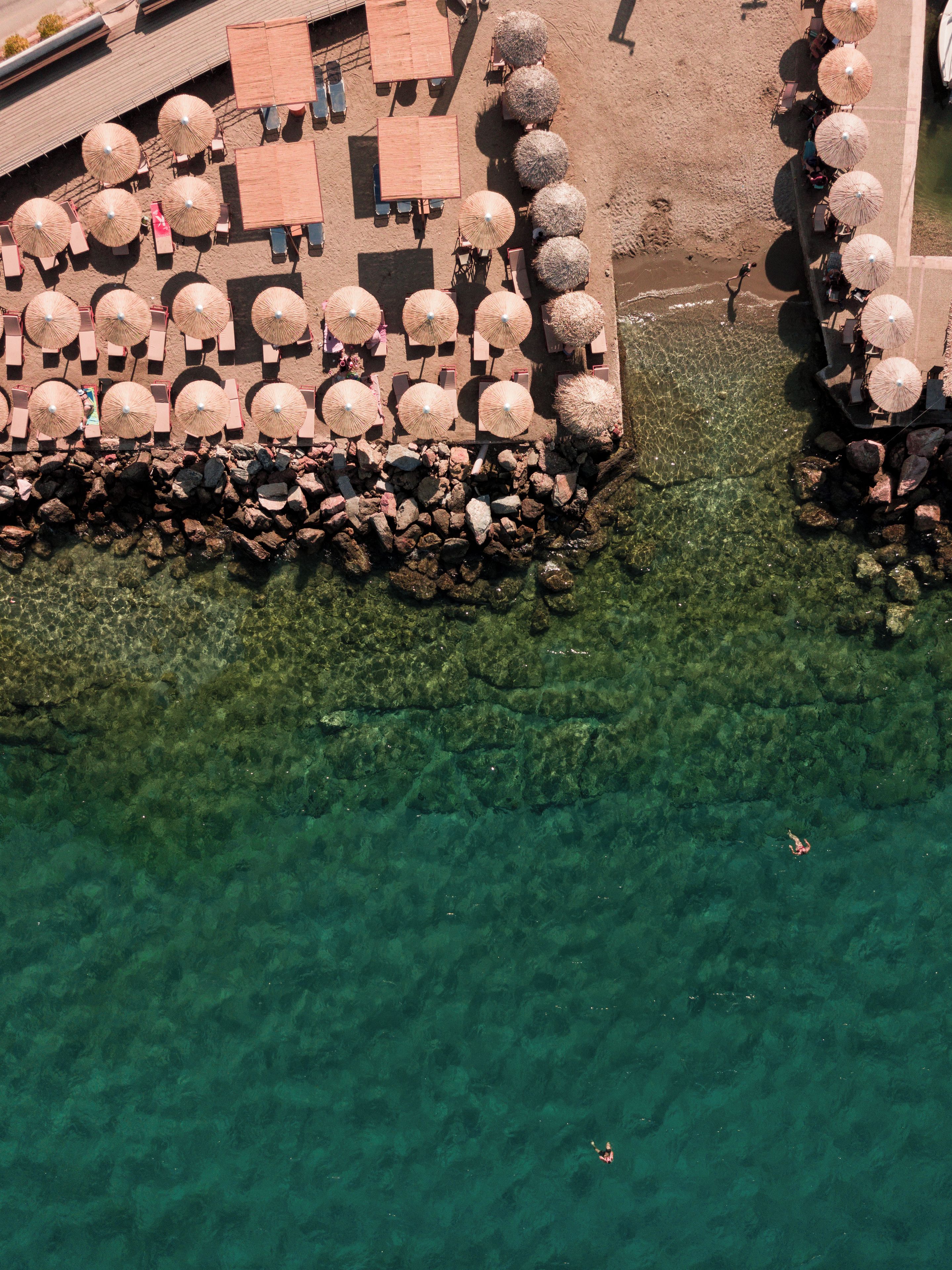 An aerial view of a beach area with clear water, umbrellas, and seating arrangements.