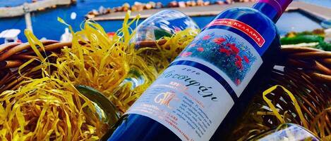 Una botella de vino con etiqueta, sobre un lecho de paja, con una vista panorámica del mar y una isla distante al fondo.