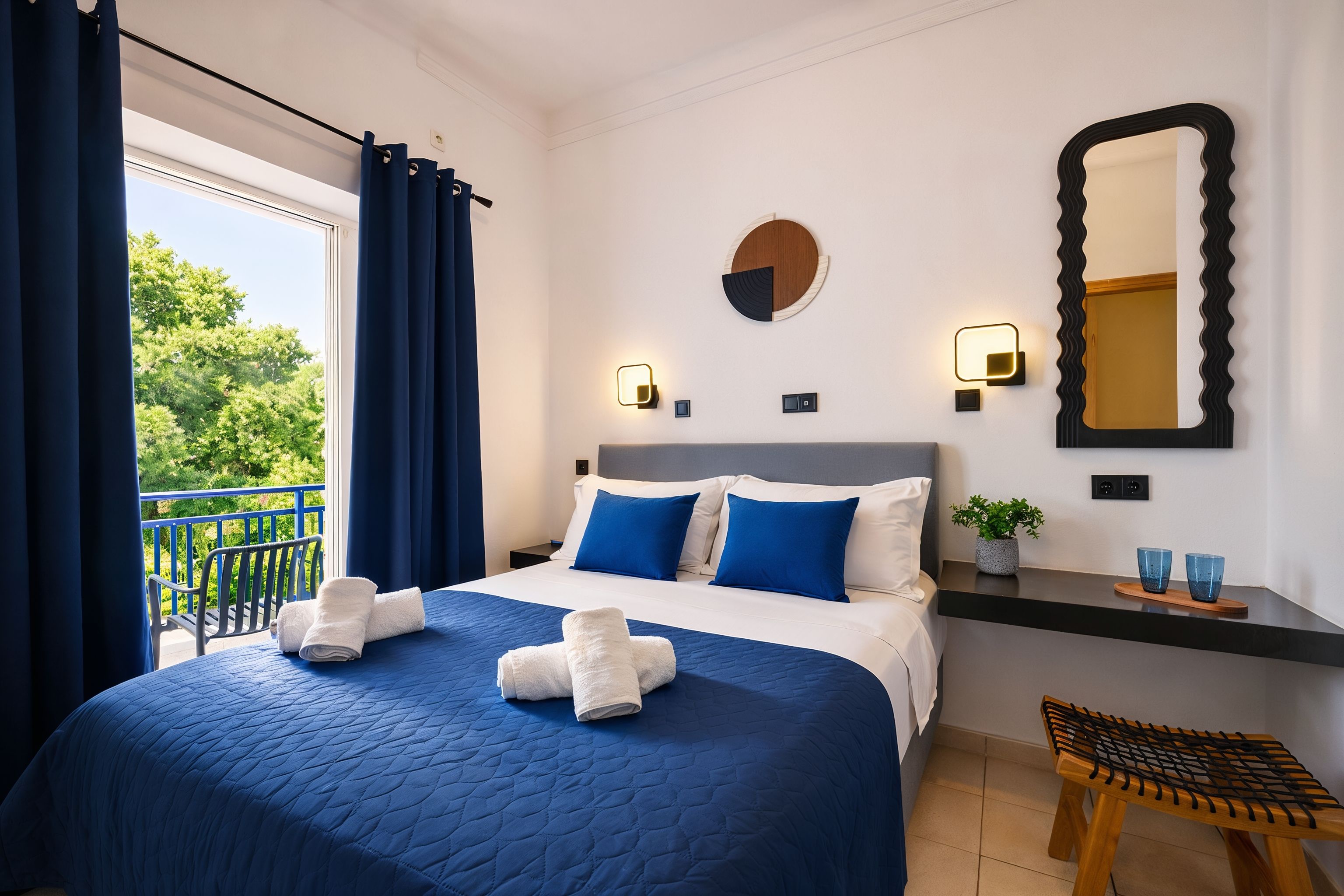 Une chambre d’hôtel avec un lit, une table de chevet, un miroir et une vue sur la verdure.
