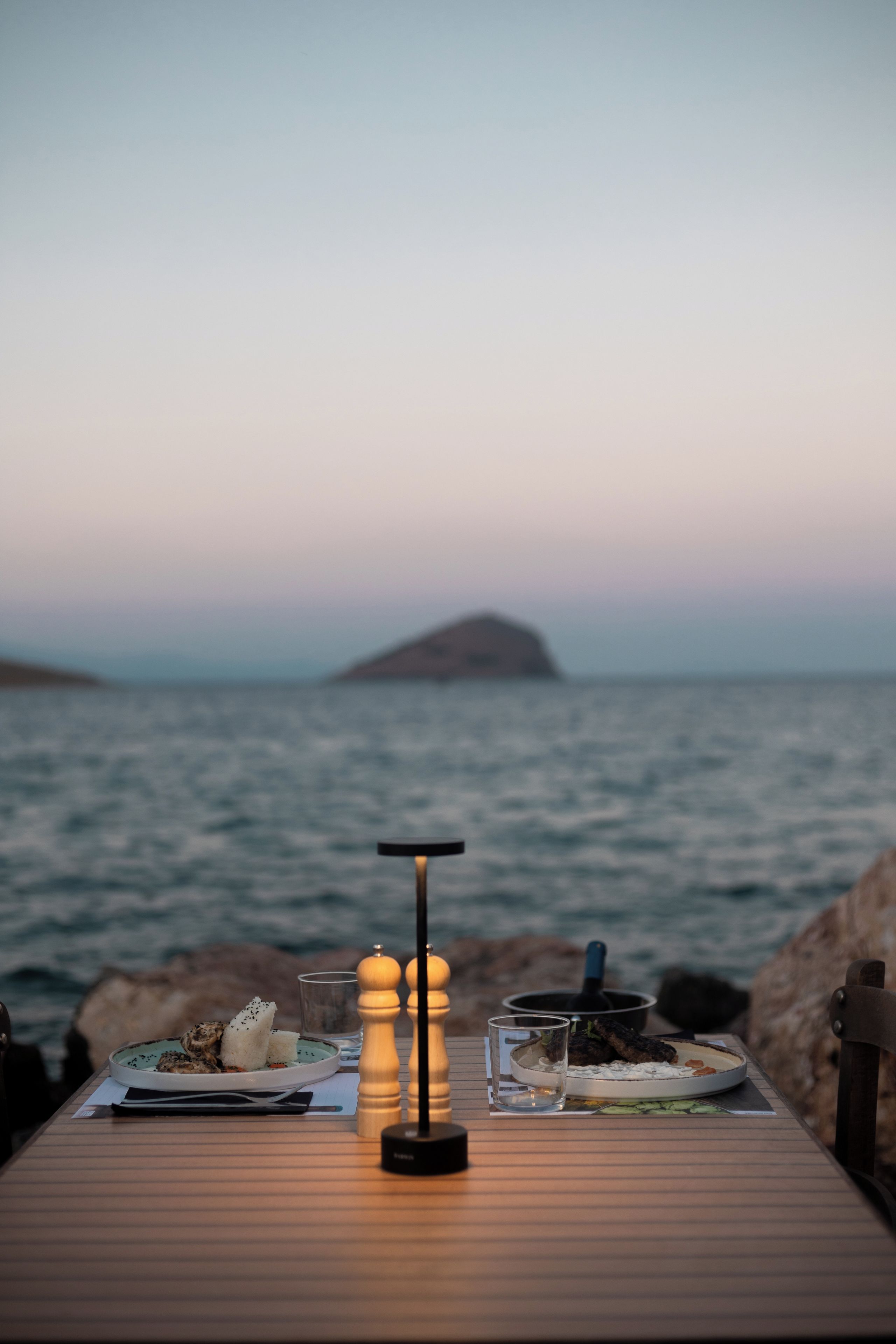 A table set for a meal with a view of the sea and a distant island.