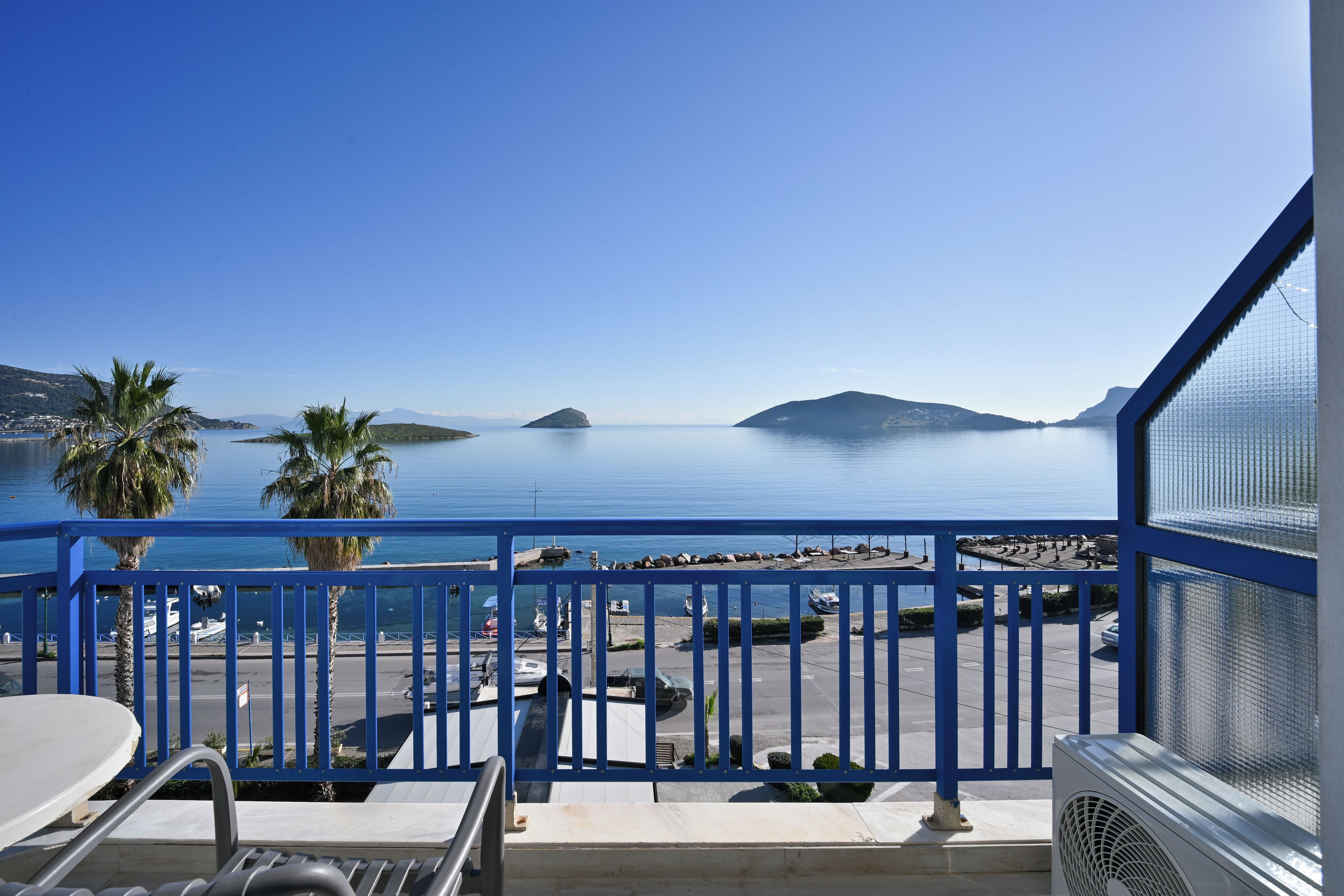 A balcony with a view of the sea, a palm tree, and a distant island.