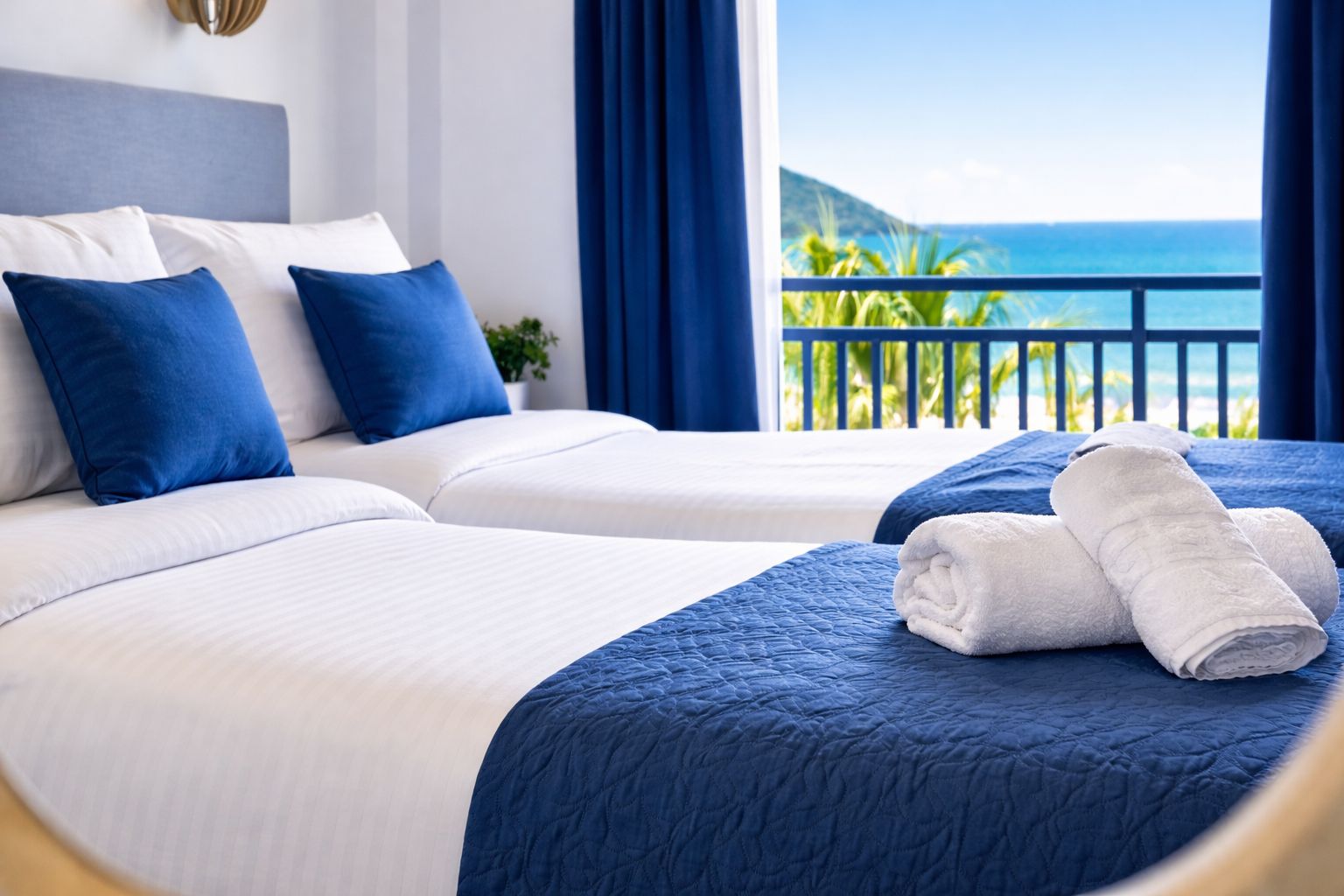 A hotel room with two beds, a view of the ocean, and a balcony with a railing.