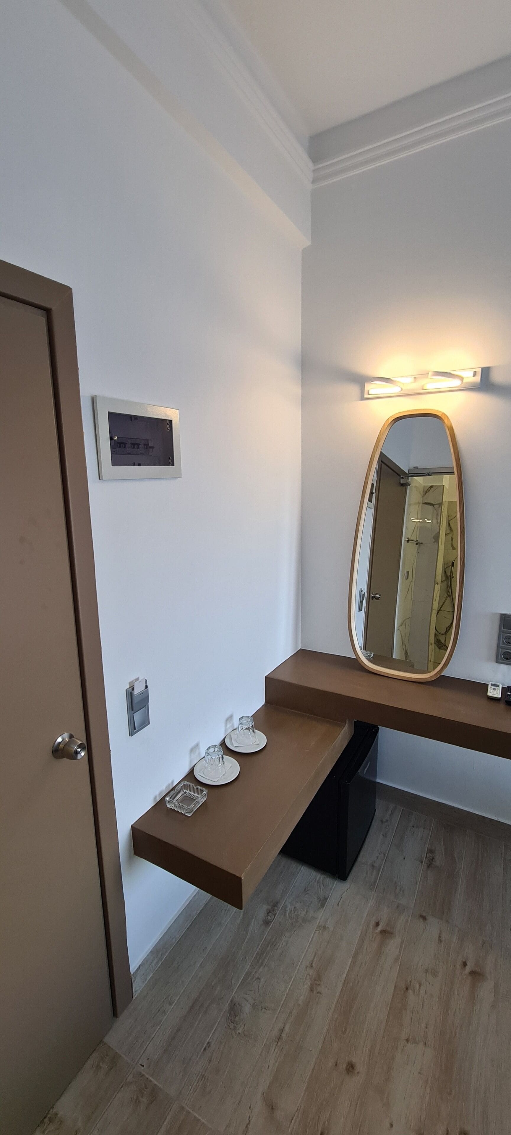 Une salle de bain avec un meuble-lavabo en bois, un miroir avec un éclairage au-dessus et une porte.