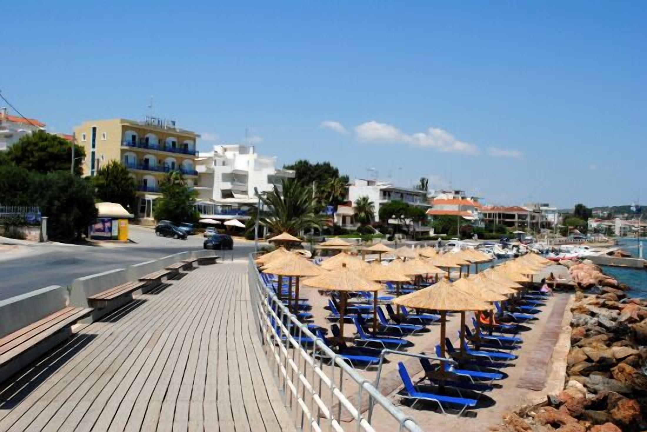 Un paseo marítimo costero con un camino de madera, sombrillas de playa y sillones azules para tomar el sol.