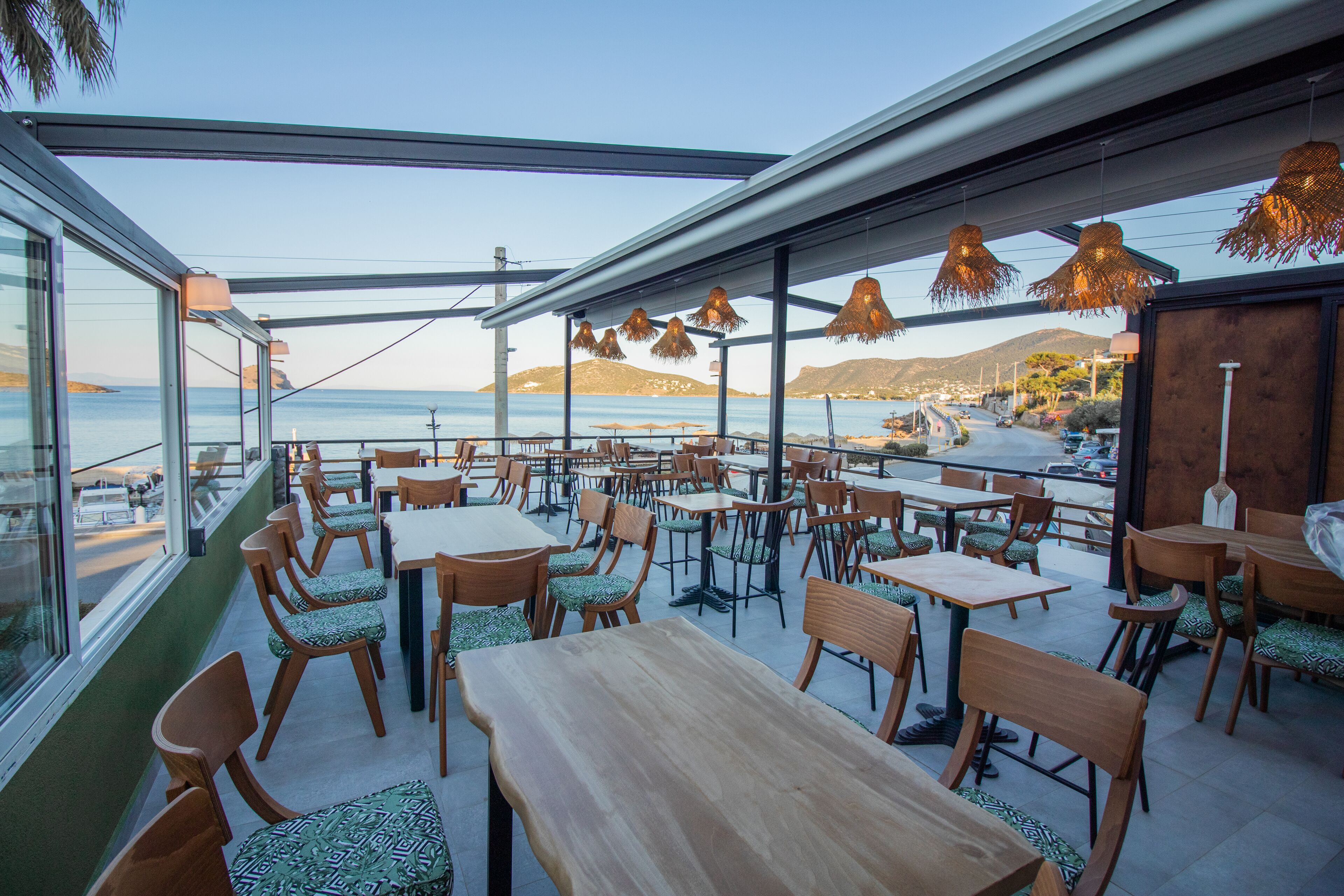 A seaside restaurant with outdoor seating, tables, and chairs, overlooking the ocean.